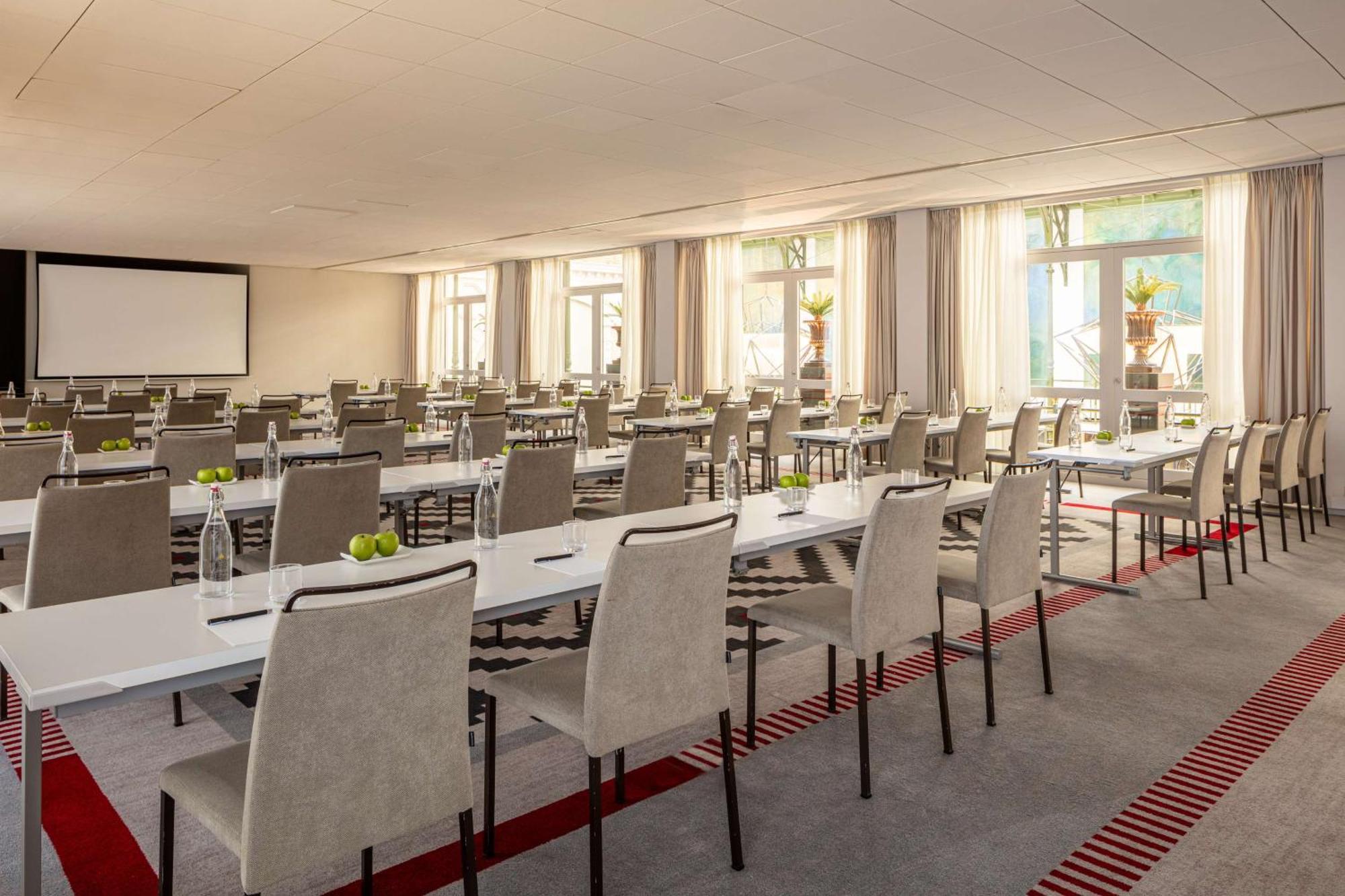 Anantara Grand Hotel Krasnapolsky Amesterdão Exterior foto The photo shows a spacious conference room or meeting space. There are several rows of long tables arranged in a structured layout, each surrounded by chairs. The tables are decorated with small items, possibly fresh fruits, and there are notepads or
